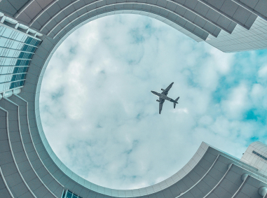 Airliner seen from directly below, framed by an airport terminal courtyard